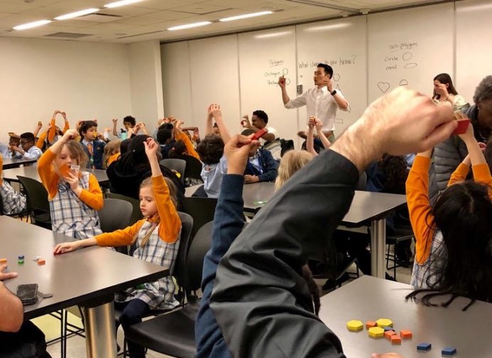 A MoMath educator running an educator session in a classroom full of children with their hands raised