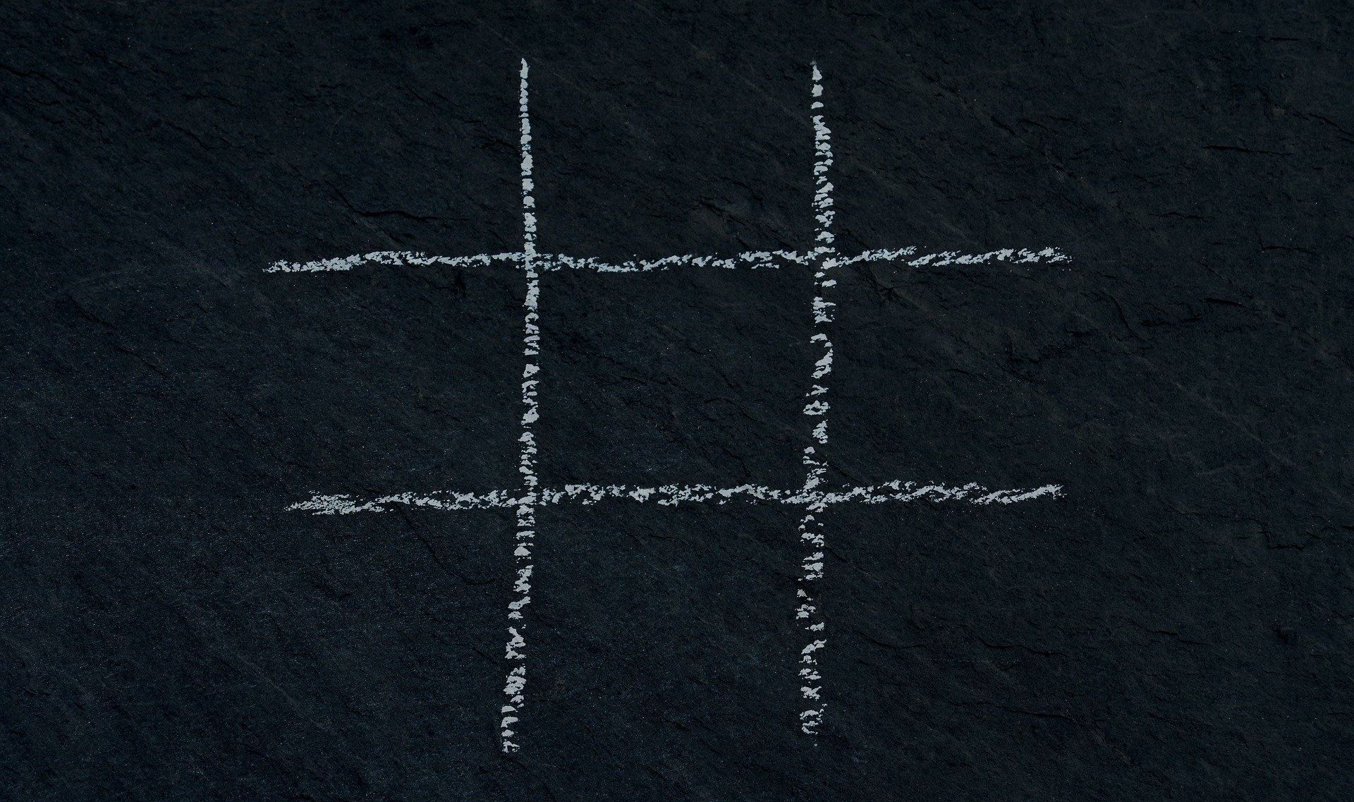 Tic tac toe grid written in chalk on a blackboard.